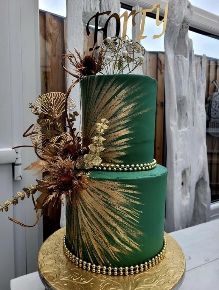 a green and gold wedding cake with flowers on the top is sitting on a table