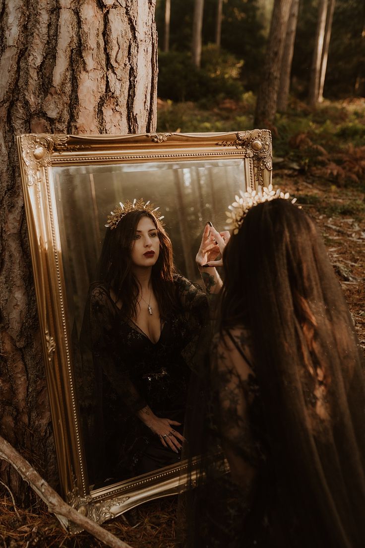 a woman standing next to a tree in front of a mirror with her reflection on it