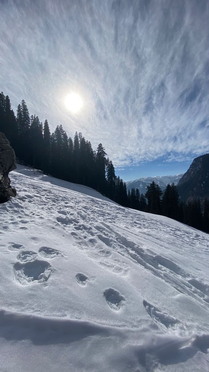 the sun shines brightly over a snow covered hill with footprints in the foreground