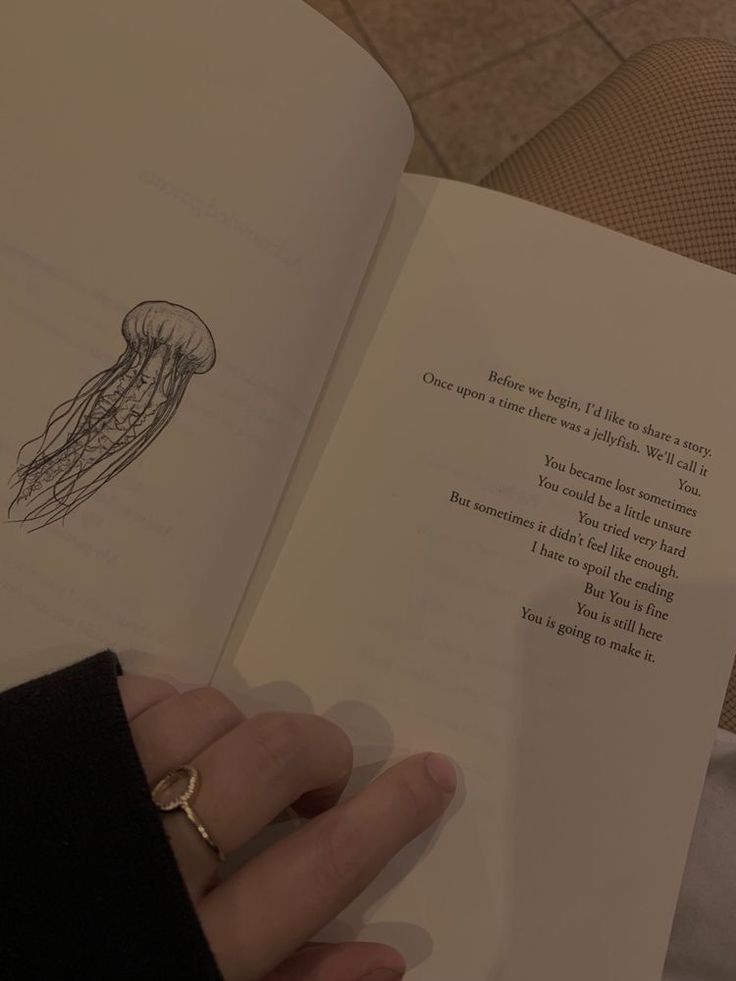 a person holding an open book with a jellyfish drawing on the page and writing in it