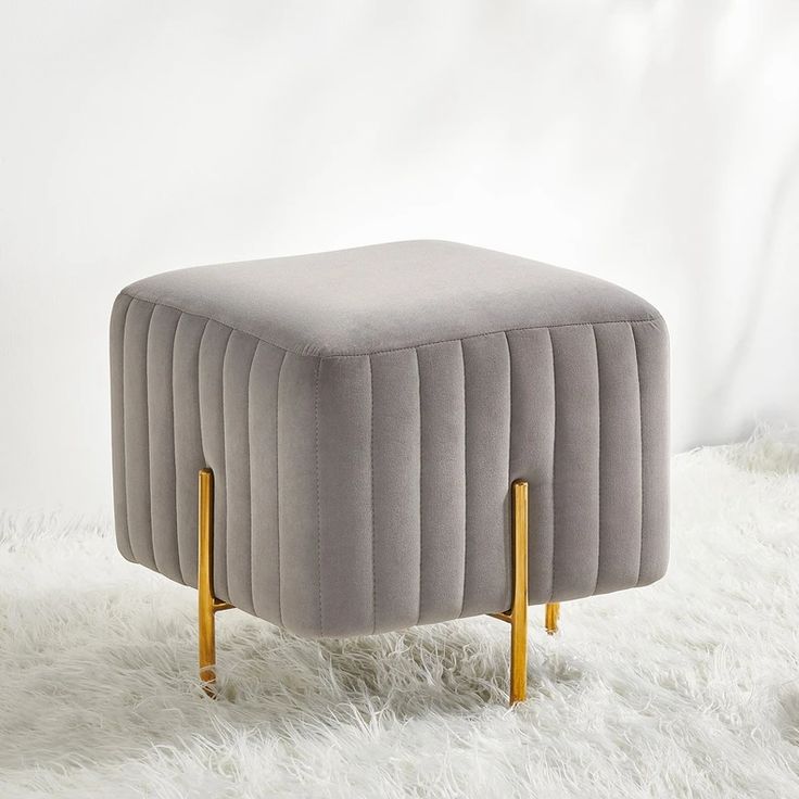 a grey ottoman sitting on top of a white fur covered floor next to a wall