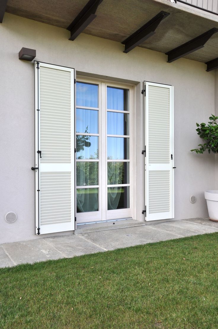 an open window on the side of a building with white shutters and green grass