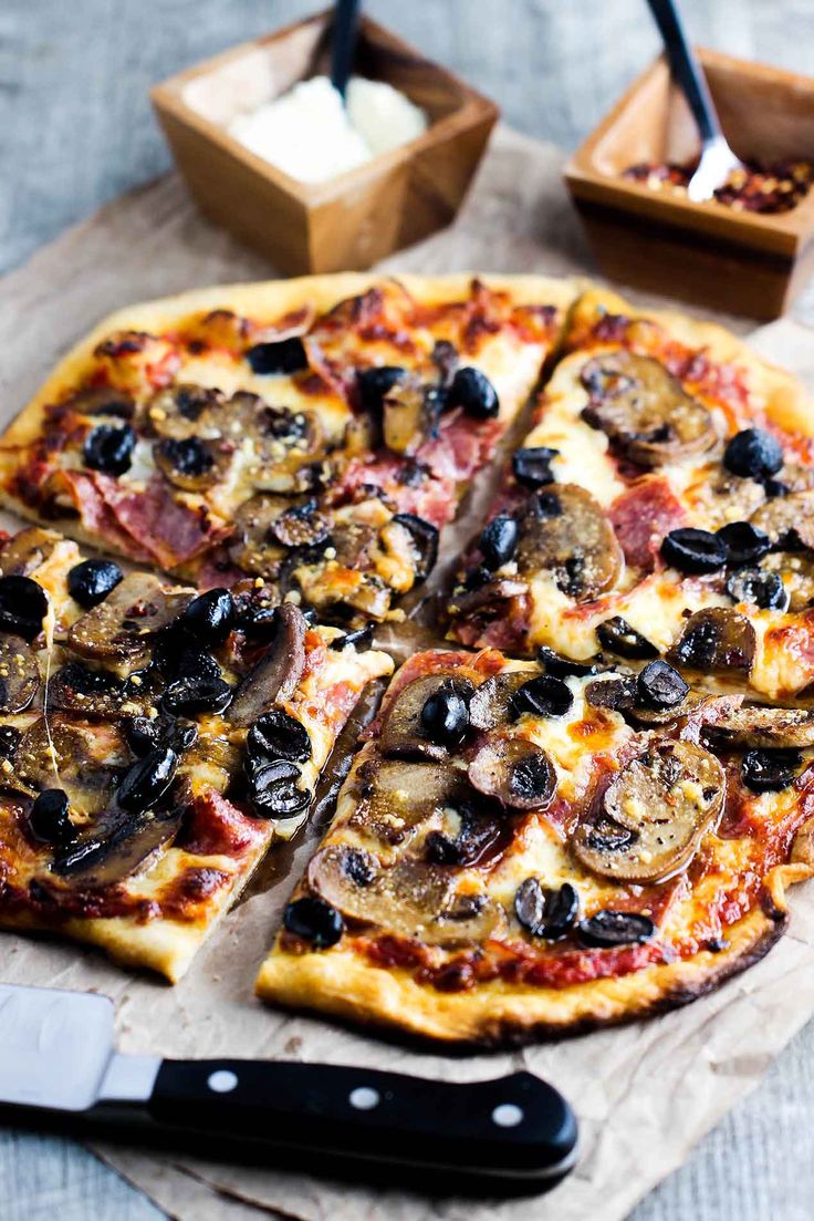 a pizza cut into four slices on top of a wooden cutting board with a knife