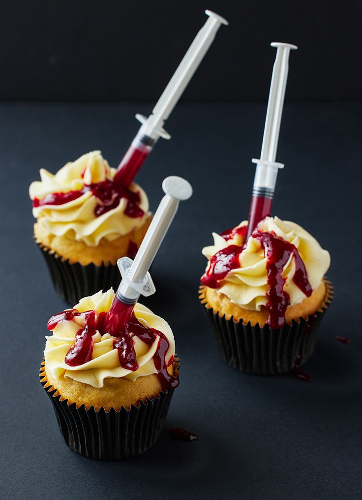 two cupcakes with blood on them and syringes stuck in the icing