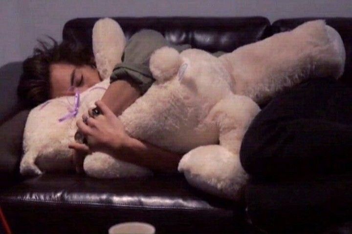 a woman is sleeping on a couch with two stuffed animals in her lap and she has one arm wrapped around the teddy bear