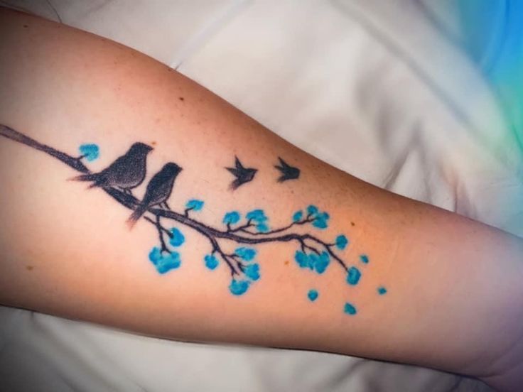 a couple of birds sitting on top of a tree branch with blue flowers around it