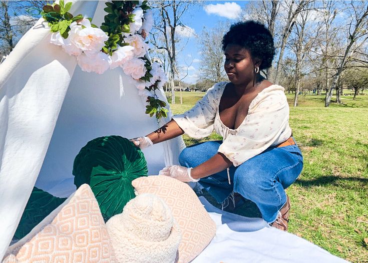 a woman is sitting on the ground with hats and flowers in front of her,