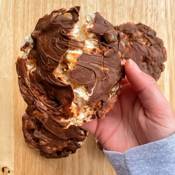 a person holding a chocolate covered cookie on top of a wooden table