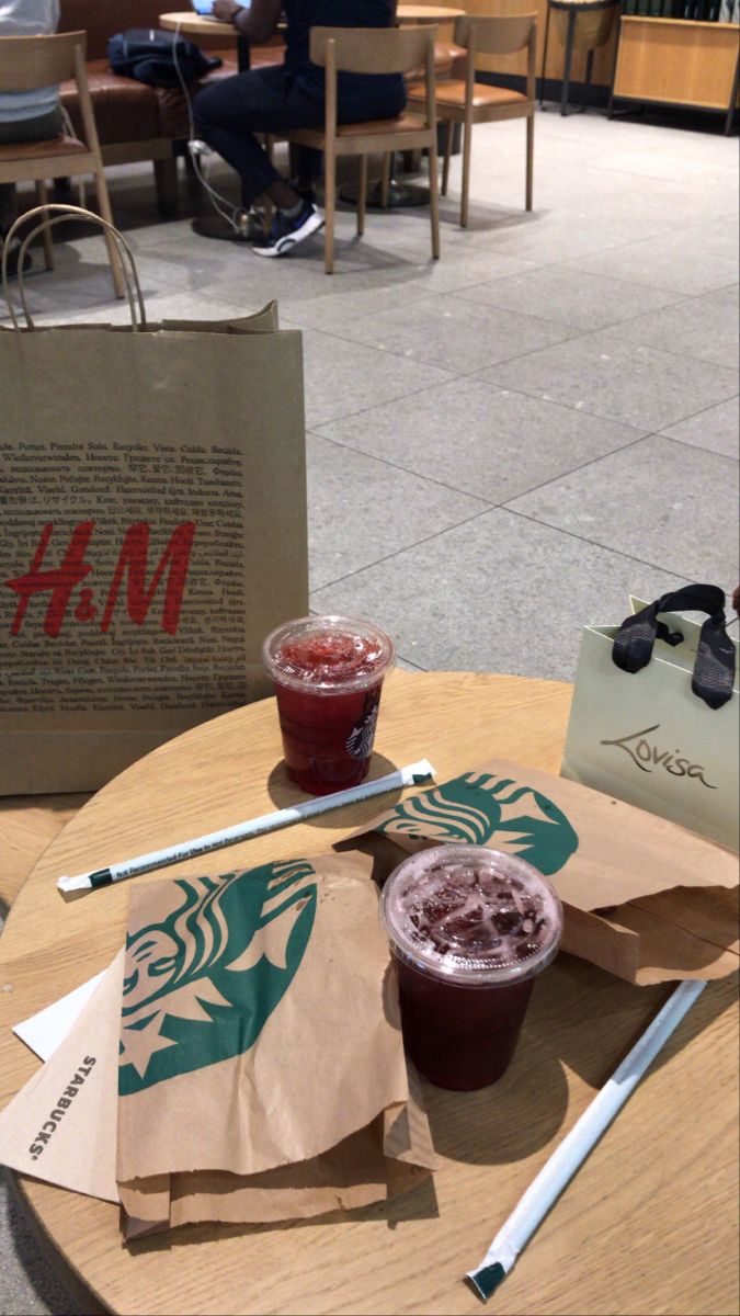 two drinks are sitting on a table with paper shopping bags and papers in front of them