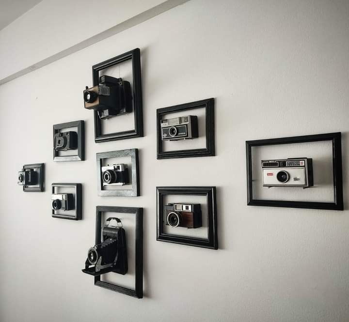 several black and white framed pictures on the wall with cameras mounted to it's sides