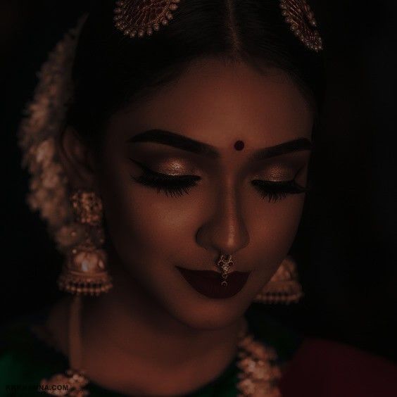 a woman with dark makeup and jewelry on her face, looking down at the camera