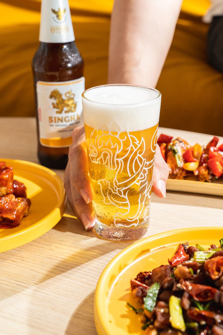 a person is holding a beer in their hand and some food on the table next to them