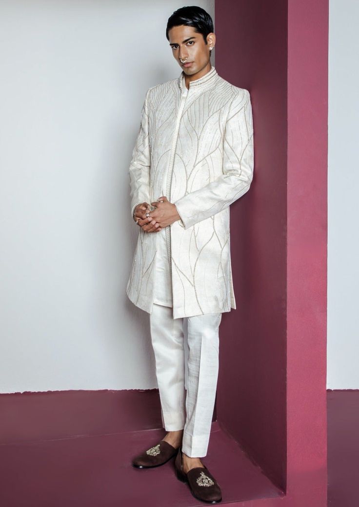 a man standing in front of a pink wall wearing a white suit and black shoes