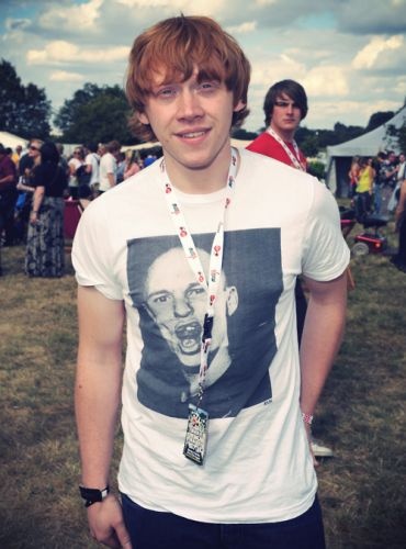 a young man standing in front of a group of people at an outdoor event wearing a t - shirt with a photo of himself on it