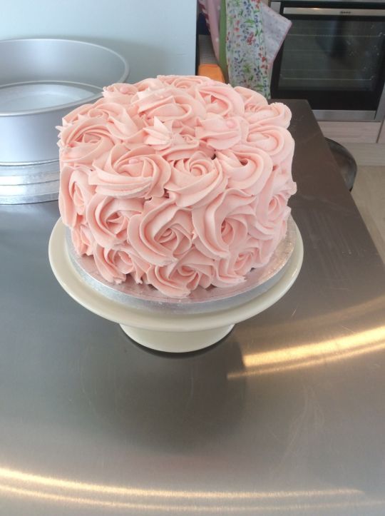 a cake with pink frosting sitting on top of a metal table next to a microwave