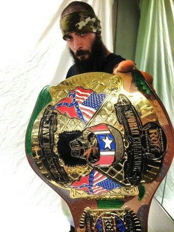 a man standing next to a giant wrestling belt in front of a curtained window