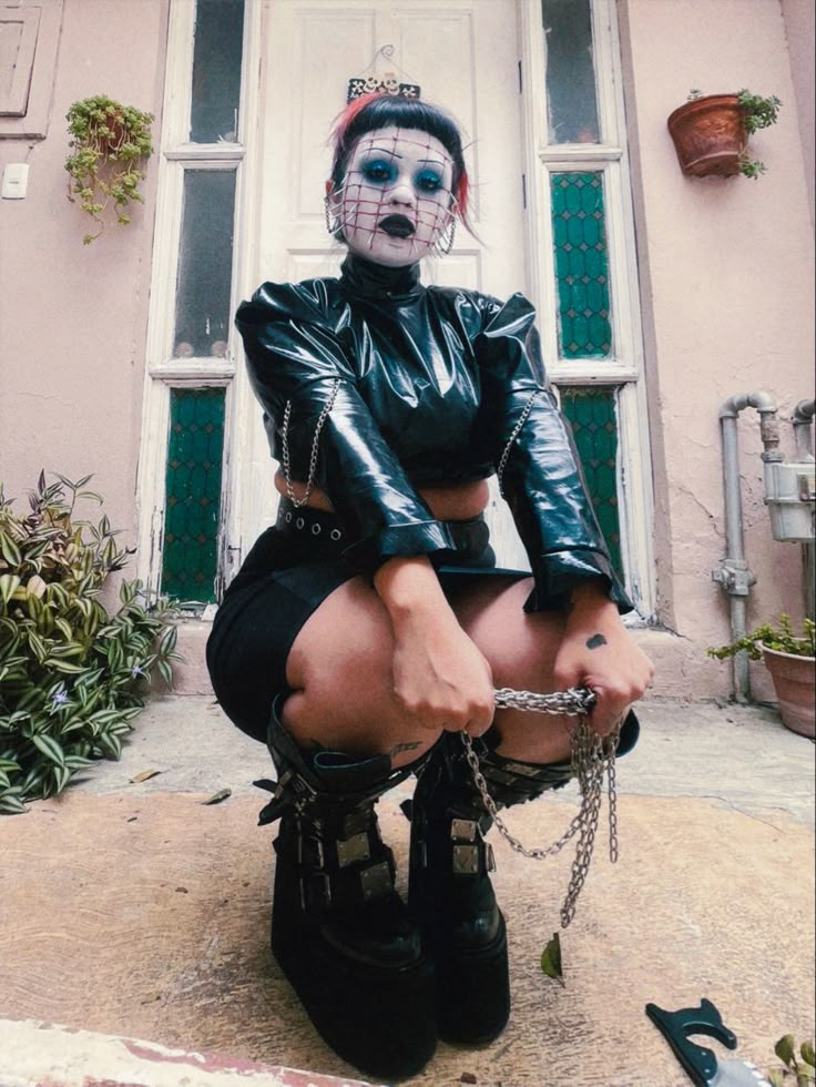 a woman in black leather outfit sitting on steps with chains around her ankles and face painted white