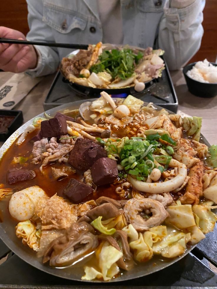 a person sitting at a table full of food with chopsticks in their hands