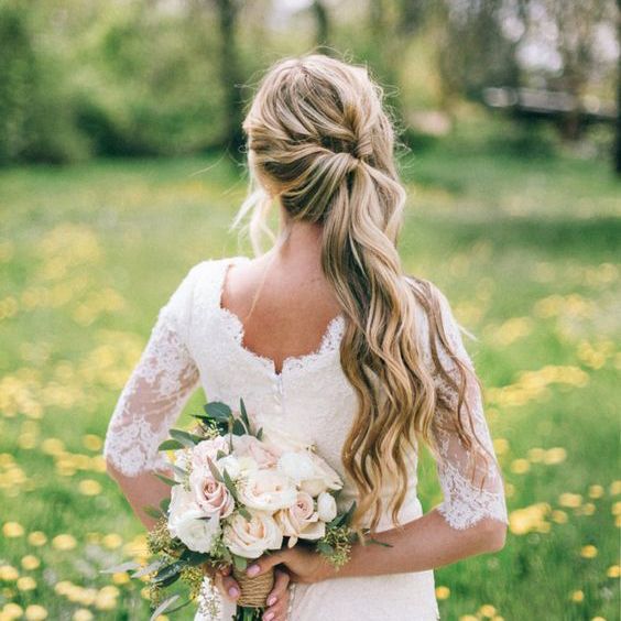 a woman standing in a field holding a bouquet of flowers and wearing a wedding dress