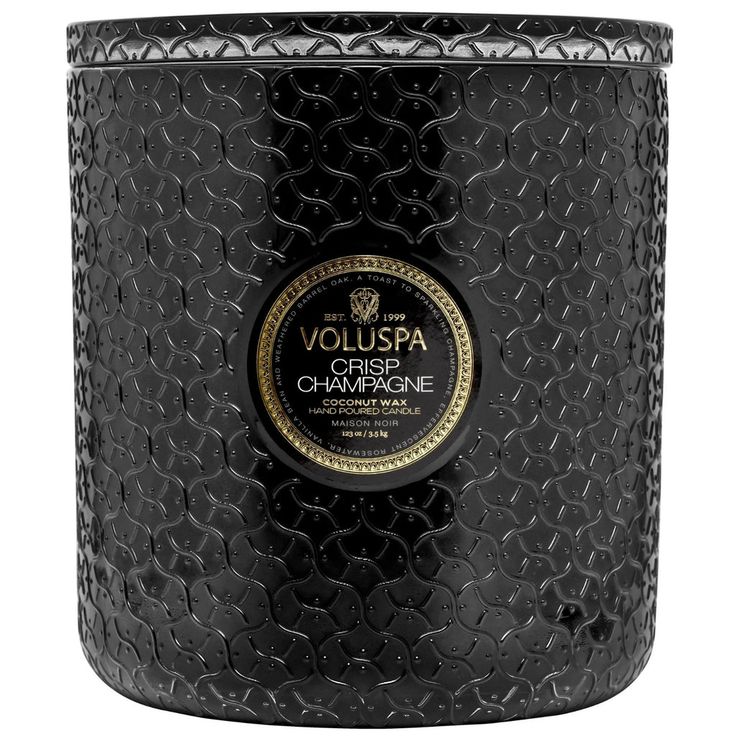 a black candle that is sitting on a white surface with the words voluspa in gold