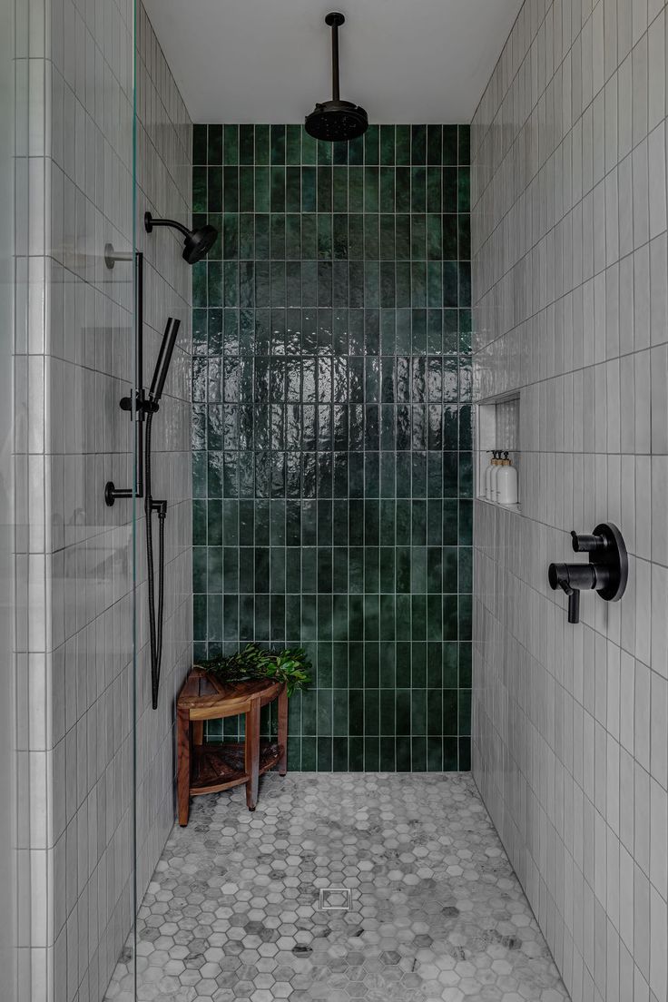 a walk in shower sitting next to a green tiled wall with a bench on the side