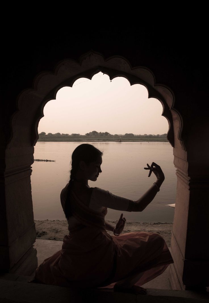 a woman sitting on the edge of a body of water with her hand up in the air