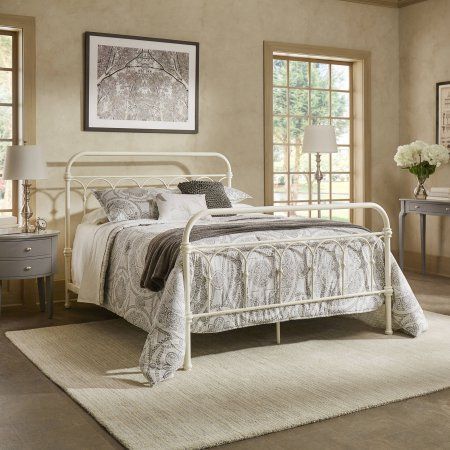 a white bed sitting in a bedroom on top of a carpeted floor next to two windows