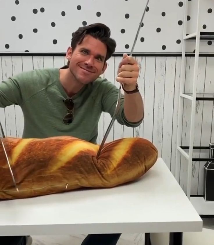 a man holding scissors over a giant loaf of bread