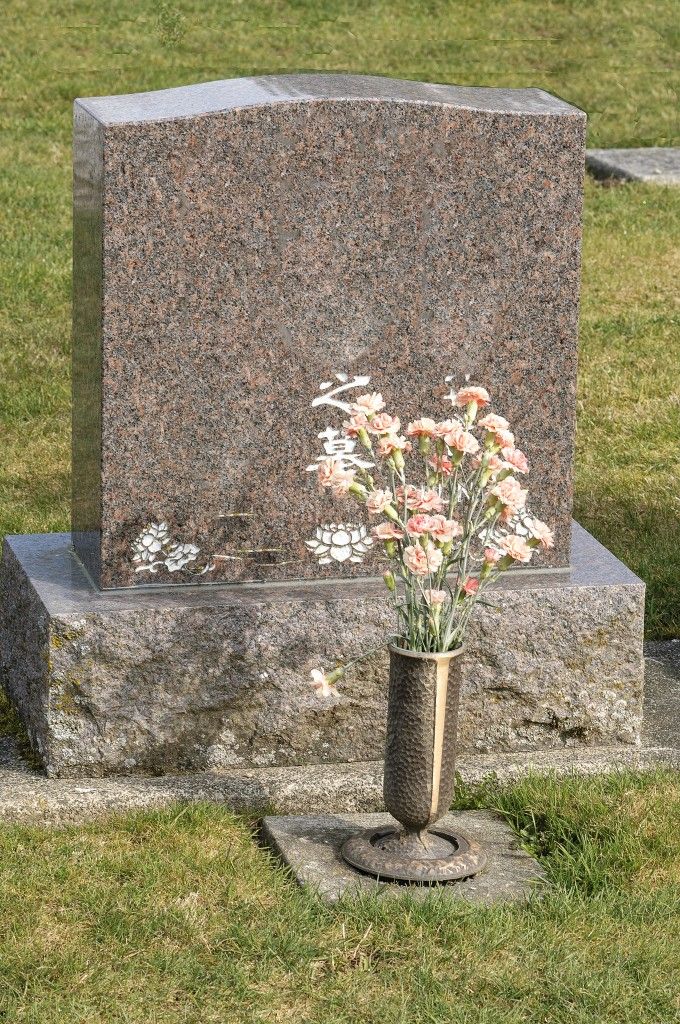 a vase with flowers in it sitting next to a stone marker on the grass covered ground