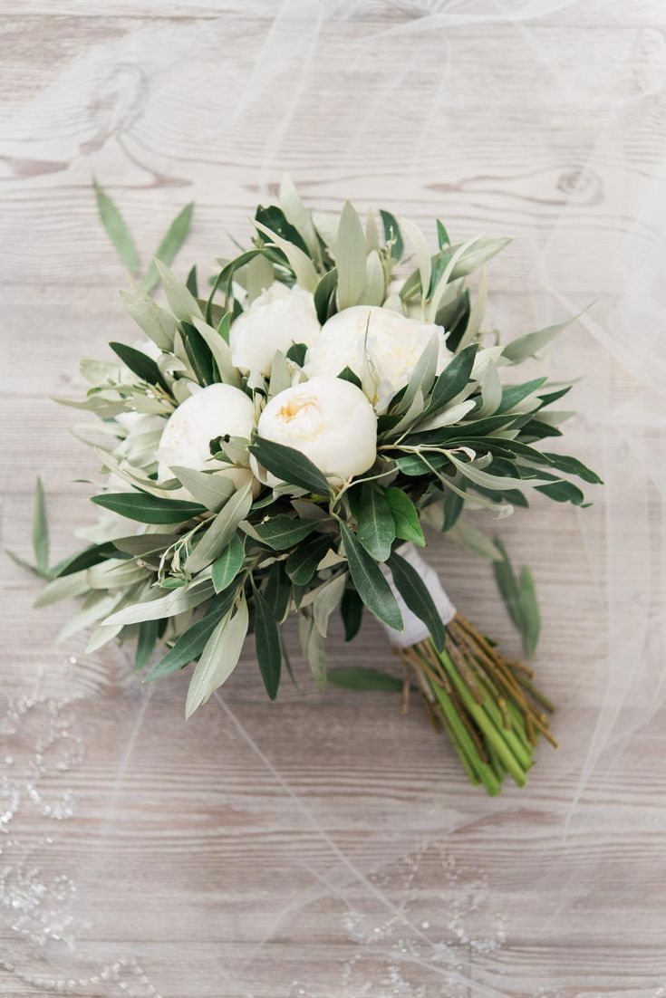 a bridal bouquet with white flowers and greenery on a wooden surface, top view