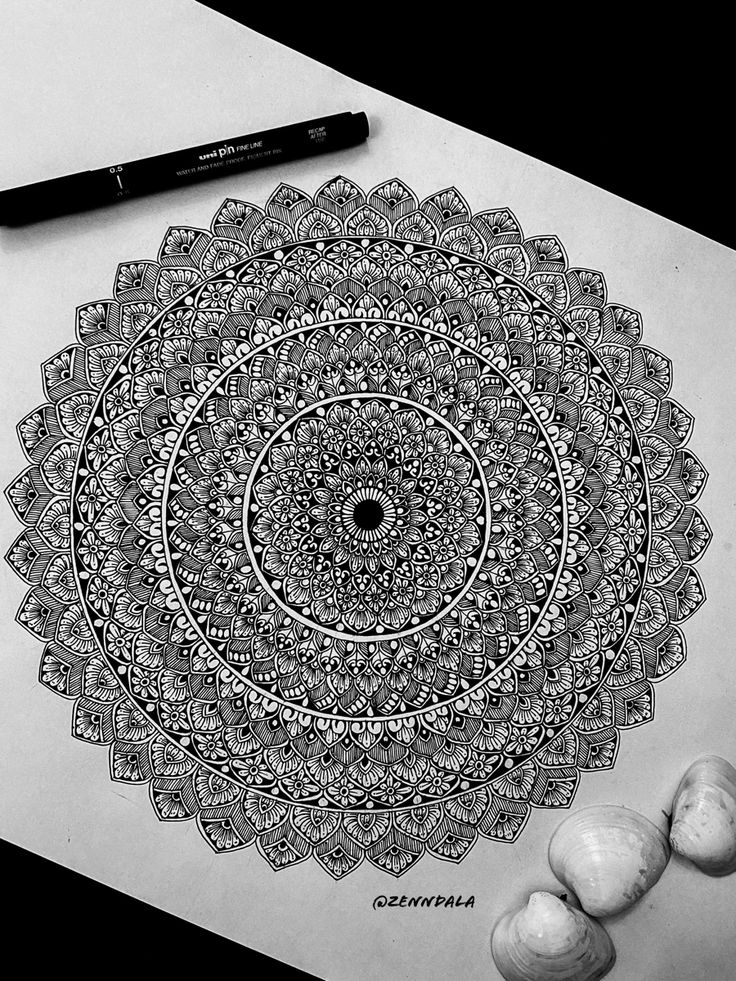 a pen and some shells on a table next to a paper with an intricate design