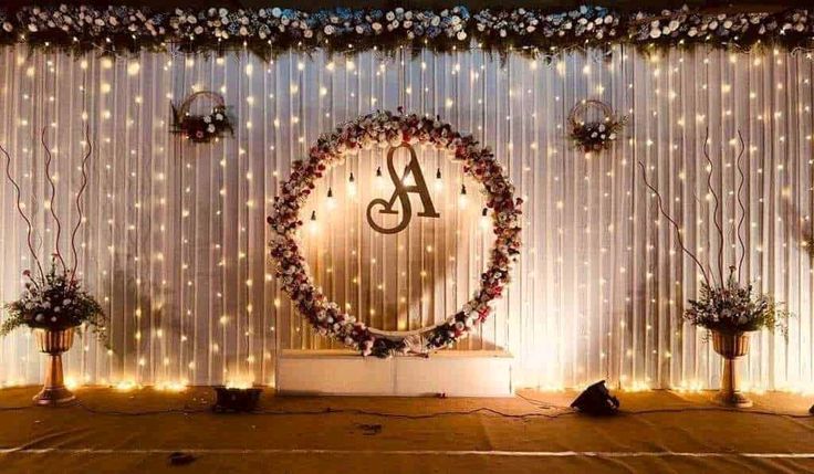 a stage decorated with flowers and lights for a wedding or reception event, complete with a monogram on the wall