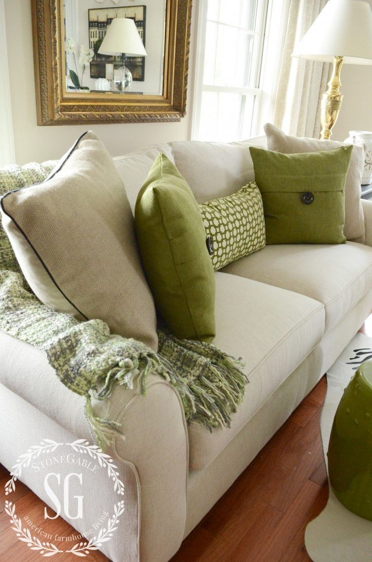 a living room with white couches and green pillows on the back of it's sofa