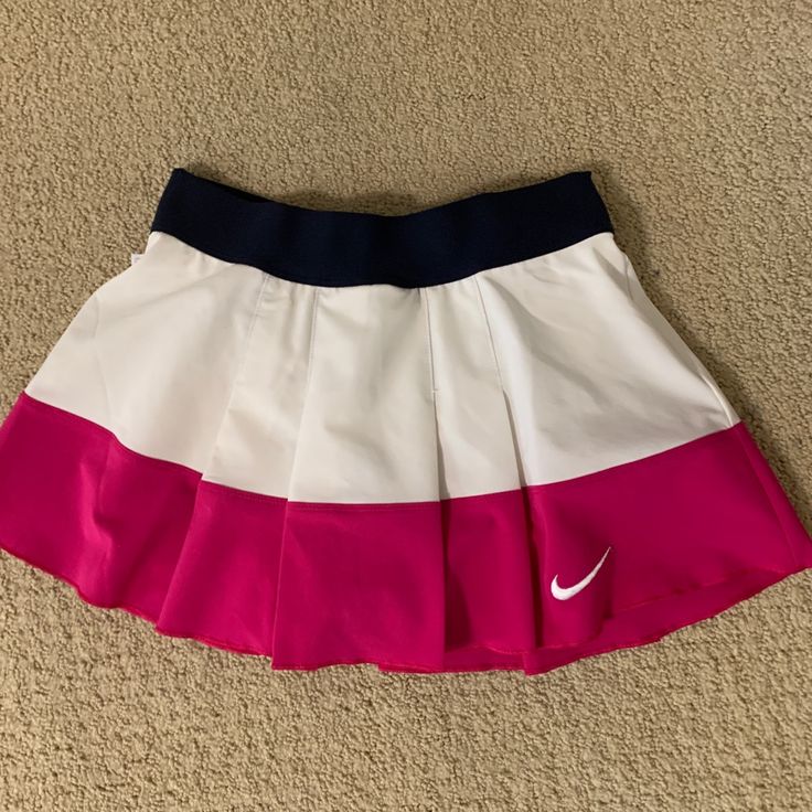 a pink and white tennis skirt on the floor next to a pair of blue shoes