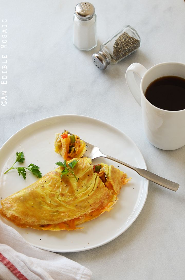 a white plate topped with an omelet next to a cup of black coffee