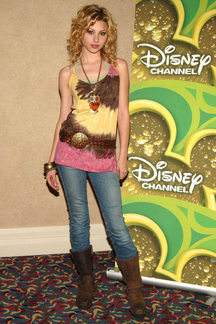 a young woman standing in front of a disney channel sign wearing cowboy boots and a tank top