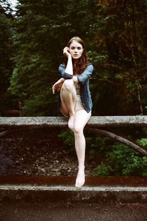 a woman is posing on a bridge in front of some trees and water with her legs spread out