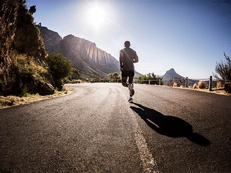 a man running down the middle of a road in the sun with mountains behind him