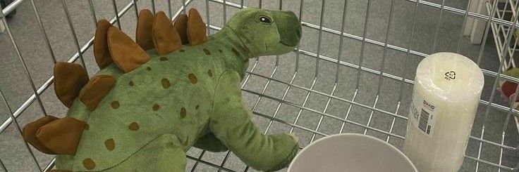 a stuffed toy dinosaur sitting next to a toilet in a shopping cart at a store