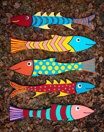 four fish painted on wooden planks laying in the grass with leaves around them,