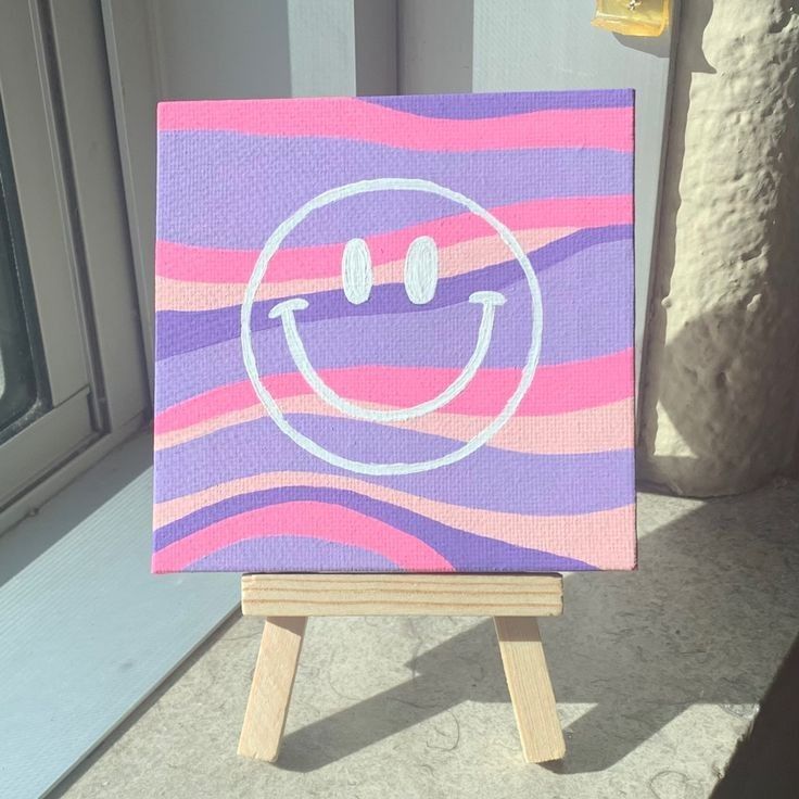 an easel with a painting on it sitting in front of a window that has a smiley face painted on it