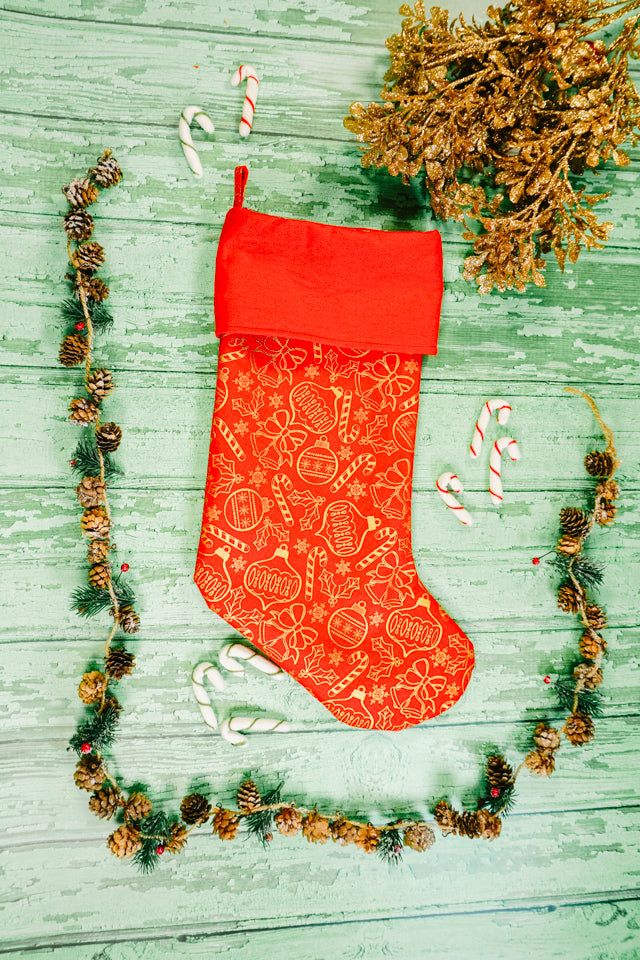 an orange christmas stocking with candy canes and pine cones on a green wooden table