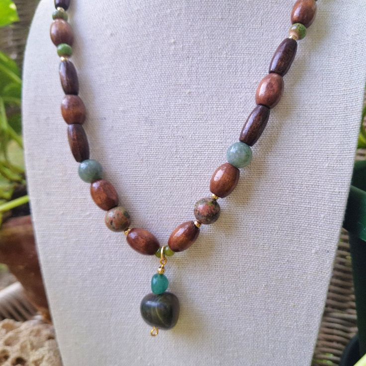 A Long Earthy Bohemian Gemstone And Wood Beaded Necklace. Crafted With Green Ceramic Beading, Natural Varnished Wood Tube And Barrel Beading, Polished Green Jade Stone, Polished Green Unakite Stone, 4 Mm Green Glass Beading, And A Unique Pendant Made Of Ocean Blue Tourmaline Stone And A Striking Tumbled Dark Green River Jasper Stone. Handmade By Me, One Of A Kind. Hypoallergenic Stainless Steel Chain And Clasp. Nickel Free. Total Length: 21 Inches Length Of Chain: 19.5 Inches Extender Length: Ha Nature-inspired Wooden Beaded Necklace As Gift, Handmade Bohemian Jade Beaded Necklaces, Jade Gemstone Beads Necklace In Nature-inspired Style, Nature-inspired Jade Necklace With Gemstone Beads, Adjustable Green Rustic Necklace, Nature-inspired Jade Gemstone Beads Necklace, Adjustable Rustic Green Necklace, Earthy Wooden Beads Necklaces Gift, Bohemian Hand-strung Jade Necklaces