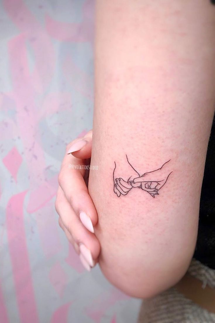 a woman's arm with two hands holding each other tattoo on her left thigh