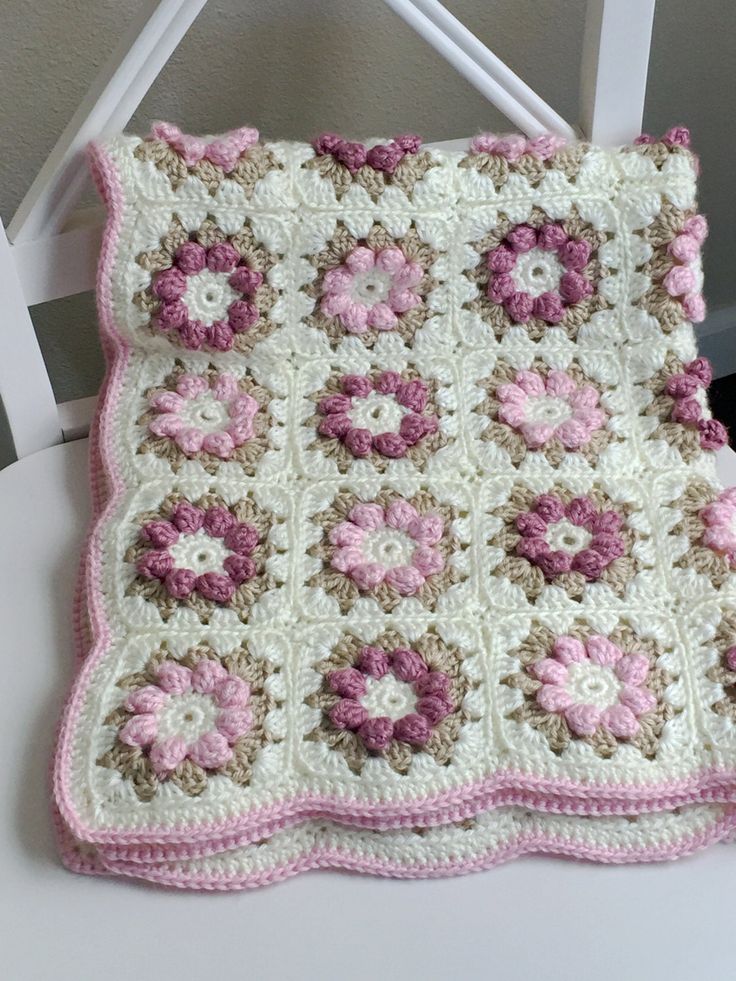 a crocheted blanket with pink and white flowers on it sitting on a chair