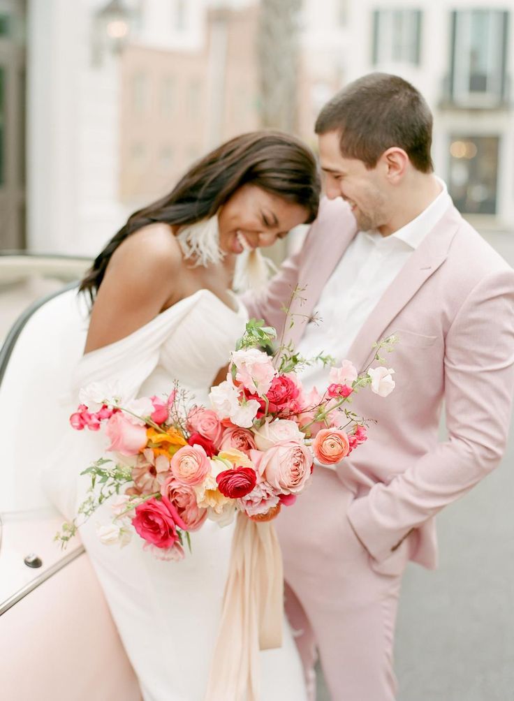 a bride and groom standing next to each other in front of a car with flowers on it