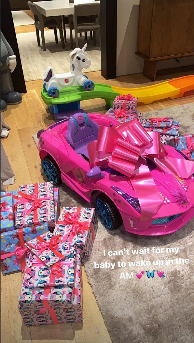 a pink toy car sitting on top of a wooden floor next to lots of presents