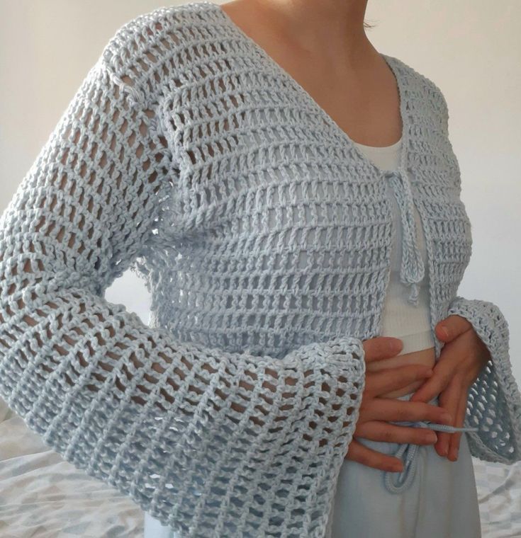 a woman is wearing a crocheted cardigan over her stomach