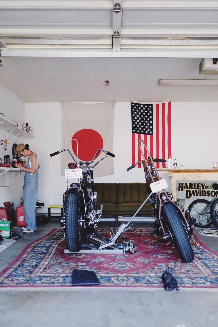 two motorcycles parked in a garage with an american flag hanging on the wall behind them