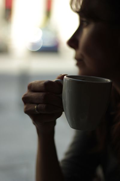 a woman holding a coffee cup in her right hand and looking at the street outside